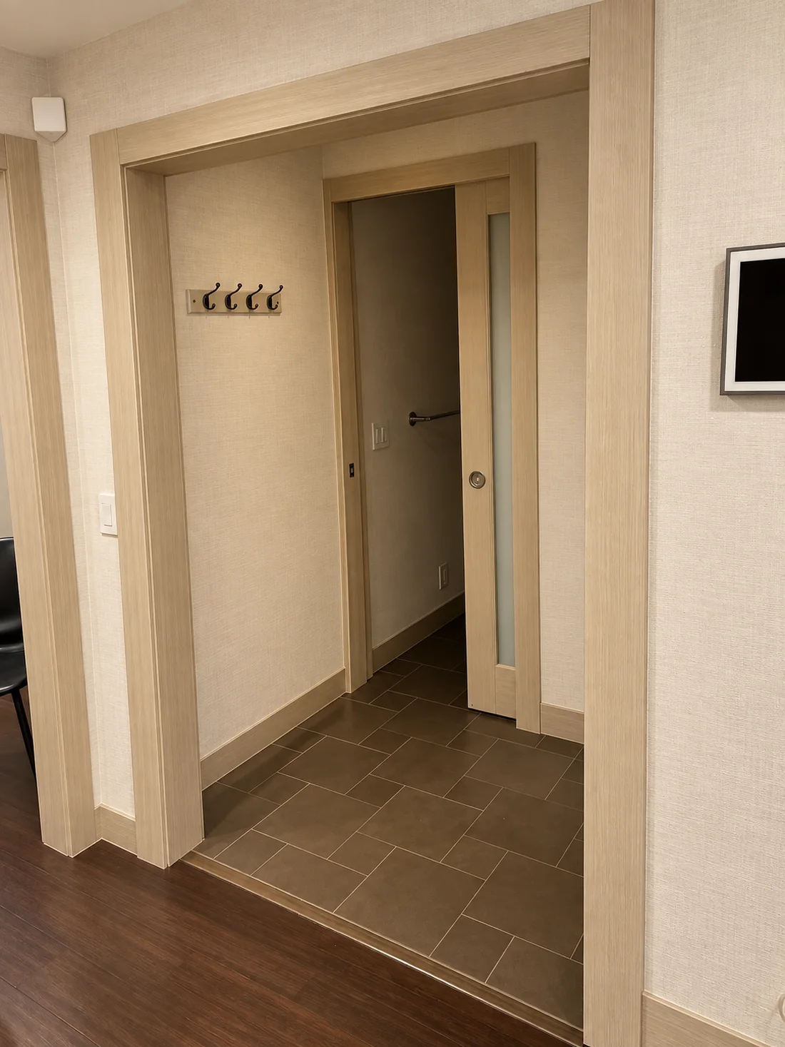 The same hallway after: walls and every casing, jamb and the pocket door wrapped in pale wood-grain and linen-texture interior film